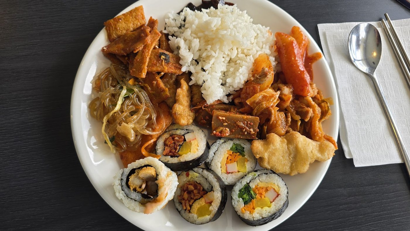 A mixed Korean meal with rice, fried pieces and rolls on one plate